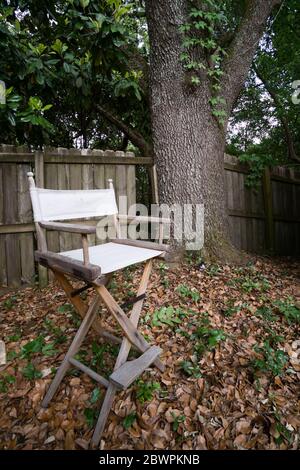 A director's chair sitting in a back yard, next to a picket fence at the edge of a wood lot in Alabama. Stock Photo