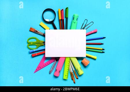 Group of School or office supplies around a notepad on light blue background. Space for text. Stock Photo