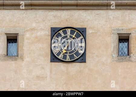 Antique round clock on the tower of Karlstejn Castle in the Czech Republic. Small windows are symmetrically located to the left and right of the clock Stock Photo