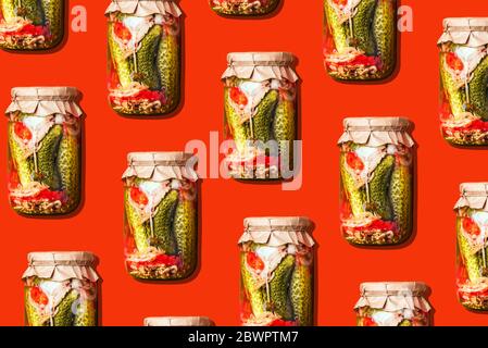 Canned and preserved vegetables in glass jars on orange background. Pickled cucumbers in jar pattern. Top view. Flat lay. Creative packing design. Hea Stock Photo