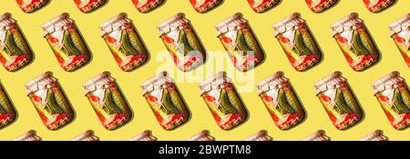 Canned and preserved vegetables in glass jars on yellow background. Pickled cucumbers in jar pattern. Top view. Flat lay. Creative packing design. Hea Stock Photo