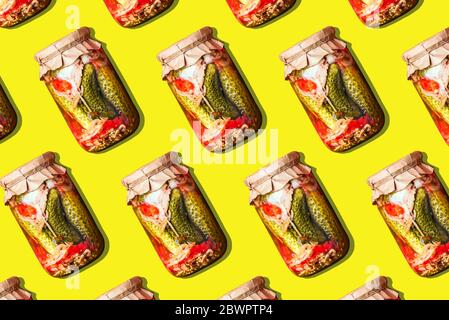 Canned and preserved vegetables in glass jars on yellow background. Pickled cucumbers in jar pattern. Top view. Flat lay. Creative packing design. Hea Stock Photo