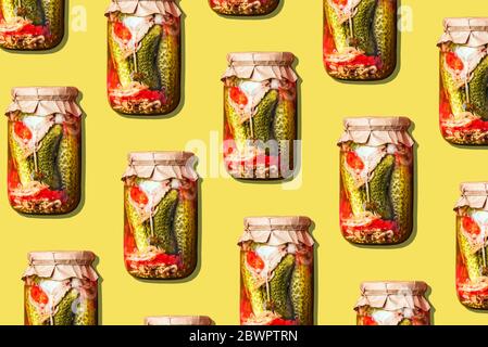 Canned and preserved vegetables in glass jars on yellow background. Pickled cucumbers in jar pattern. Top view. Flat lay. Creative packing design. Hea Stock Photo