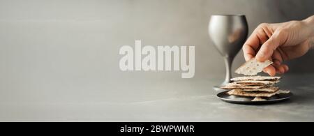 Hands with chalice and communion matzo bread, wooden cross on grey ...
