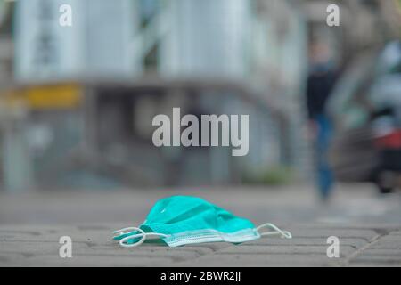 Discarded medical face mask lies on the sidewalk. Face masks polluting streets of the city since Coronavirus COVID-19. Soft focus. Stock Photo