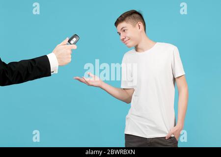 A teenager happily accepts a car key, which a man in a jacket holds out to him. Perhaps the father allows his son to drive a car. Isolated on blue Stock Photo
