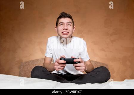 A boy in a white T-shirt enthusiastically plays a video game using a modified joystick without identification marks Stock Photo