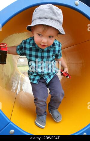 Little boy, two years old, happily playing in a tunnel in the playground at Manor Farm Country Park, Hampshire, England, UK.  MODEL RELEASED Stock Photo
