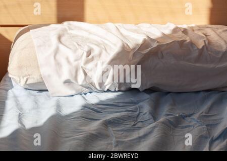 Wake up concept: pillow on unmade bed with wrinkles on sheets lit by morning window light Stock Photo