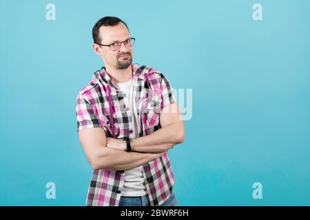 Young smiling guy with a beard in glasses and a klepy shirt folded his arms over his chest Stock Photo