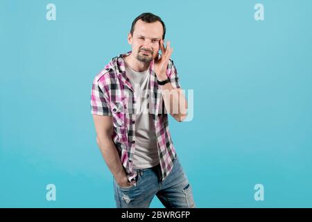 a young man with stubble in a clerical shirt pulls a corner of his eye to the side, trying to focus his poor eyesight on something. The guy forgot his Stock Photo