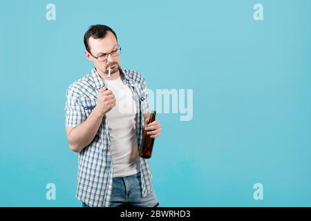 a man lights a cigarette, holding a bottle of beer in his hand and squinting to the side, as if he was being offered something Stock Photo