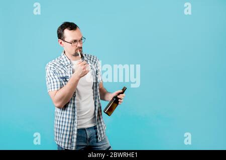 man lights a cigarette, holding a bottle of beer, but something distracted him and he looks away Stock Photo