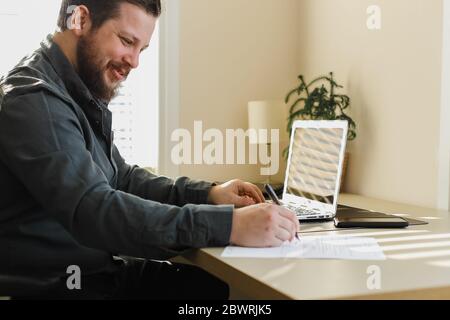 Businessman writing letter of resignation and using laptop. Stock Photo