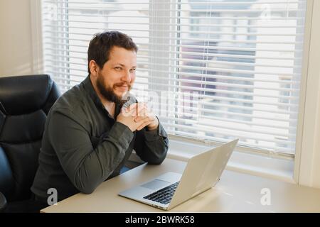 Smiling computer hacker working online with laptop at cabinet. Stock Photo