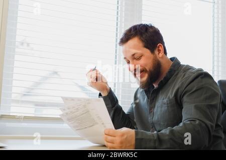 Successful financier reading and filling documents at office near window. Stock Photo