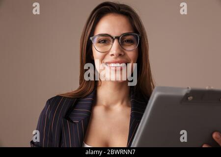 Photo of cheerful businesswoman in eyeglasses smiling and posing with clipboard isolated over grey background Stock Photo