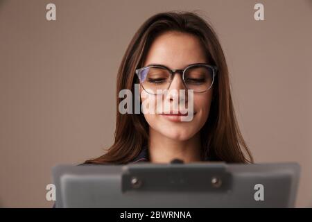 Photo of focused businesswoman in eyeglasses posing with clipboard isolated over grey background Stock Photo