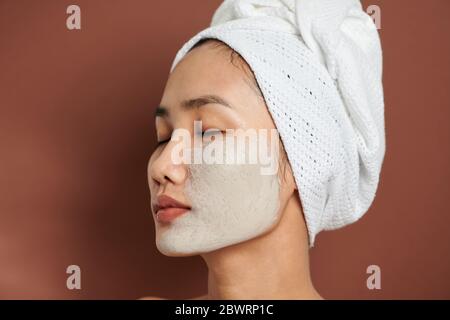 Close up shot of beautiful Asian woman applies purifying mask on face, has beauty treatments Stock Photo