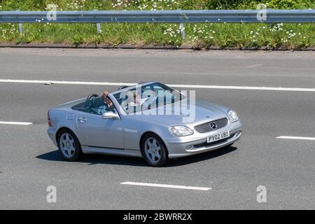 2002 silver Mercedes Benz SLK 230 Kompressor Auto; Vehicular traffic moving vehicles, convertible, convertibles, soft-top, open-topped, roadster, cabriolets, drop-tops cars driving vehicle on UK roads, motors, motoring on the M6 motorway Stock Photo