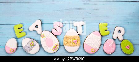 Sweets for celebrate Easter. Gingerbread in shape of easter eggs and letter Easter. Blue background top view copy space Stock Photo