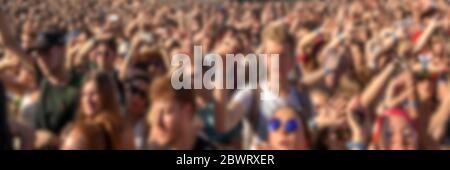 Blurred crowd of young people with arms raised in summer. Outdoor event, panoramic background. Stock Photo