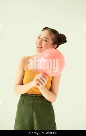 Happy cheerful Asian girl holding pink air balloon over light background. Stock Photo