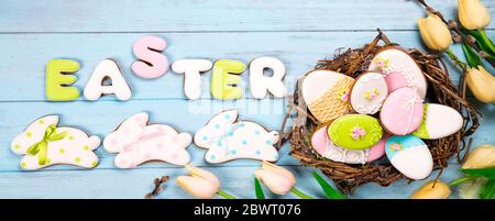 Beautiful white tulips with colorful quail eggs in nest and cookies lettering Happy Easter and as bunny on blue wooden background. Spring and Easter h Stock Photo