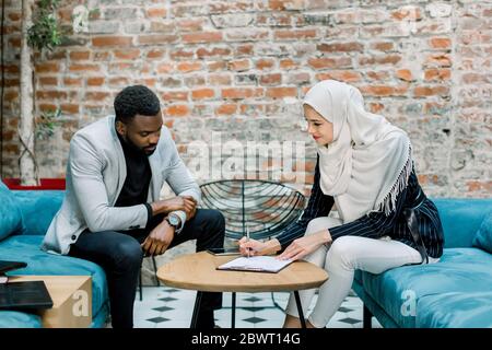 Business contract, agreement signed, co-investment business concept. Charming Muslim business lady in white hijab signing the contract, while sitting Stock Photo