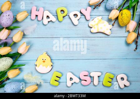 Happy Easter colorful lettering Happy Easter of ginger biscuits and cookies bunny with tulips and eggs on wooden blue background. Easter background or Stock Photo