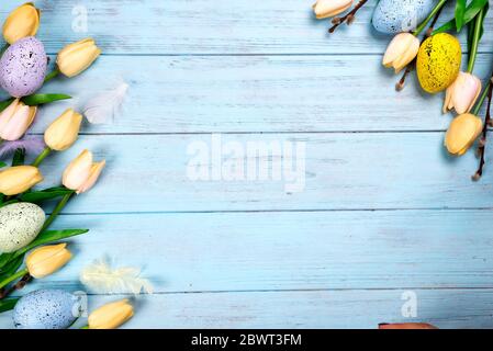 Frame of Sweets for celebrate Easter. Gingerbread in shape of easter chicken, colorful eggs and tulips. Blue background top view copy space Stock Photo