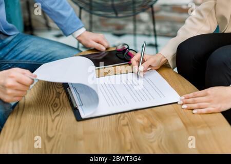 Close up cropped image of hands of two business people, man and woman, sitting at the table in modern office, signing contract, making a deal, classic Stock Photo
