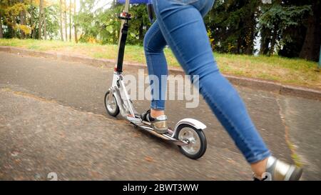 Closeup image of young woman riding fast on kick scooter at park Stock Photo