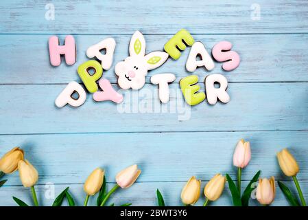 Happy Easter colorful lettering Happy Easter of ginger biscuits and cookies bunny with tulips and eggs on wooden blue background. Easter background or Stock Photo