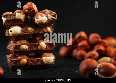 Chocolate with hazelnuts in the form of a tower on a dark background, surrounded by nuts in the shell and peeled. Stock Photo