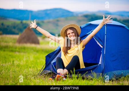 girl tourist meets morning with outstretched arms in tent with beautiful mountains view. solitude with nature Stock Photo