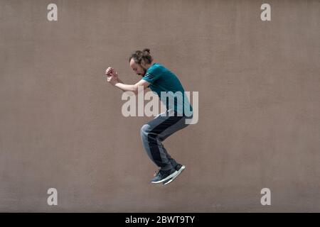 young bearded guy sortsman jumping on the background of a pink street wall. Portrait of a bearded guy of thirty years old, in sportswear, jumping high Stock Photo
