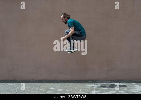 young bearded guy sortsman jumping on the background of a pink street wall. Portrait of a bearded guy of thirty years old, in sportswear, jumping high Stock Photo