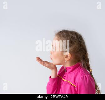 Side shot of a nice serious little girl with cute pigtails blowing a kiss to someone aside. Close up studio portrait isolated on white Stock Photo