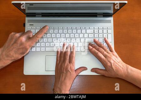 Top view of hands of old people using a laptop and pointing the computer screen. Elderly people and technology. Couple using a computer. Stock Photo