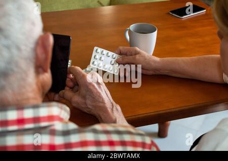 Elderly couple consulting medical questions online using the phone at home. Old people using technology to find information about medications. Stock Photo