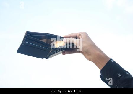 Man hand holding black empty purse isolated on sky background. Stock Photo