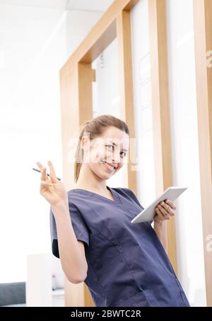 Low angle of young woman in scrubs smiling and browsing data on smartphone while working in contemporary clinic Stock Photo