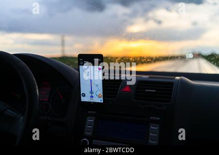 Using waze maps application on smartphone on car dashboard, Driver using maps app for showing the right route through the traffic of city at sunset on Stock Photo