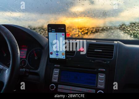 Using waze maps application on smartphone on car dashboard, Driver using maps app for showing the right route through the traffic of city at sunset on Stock Photo