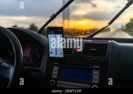 Using waze maps application on smartphone on car dashboard, Driver using maps app for showing the right route through the traffic of city at sunset on Stock Photo