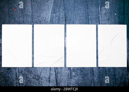 Closeup of grungy dark painted urban wall texture with four wrinkled glued poster templates. Modern mockup for design presentation with clipping path. Stock Photo