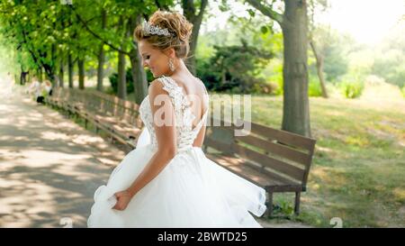Rear view photo of happy smiling young bride walking away from camera in park Stock Photo