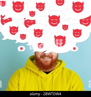What's in your head. Young man with big speech bubbles on his head like a hairstyle made of devil's smiles. Creative contemporary artwork. Daily thoughts, bulling, abusing, bad thoughts visible. Stock Photo