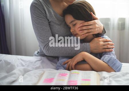 Mother and her daughter reading from bible and praying in their knees near the bed Stock Photo